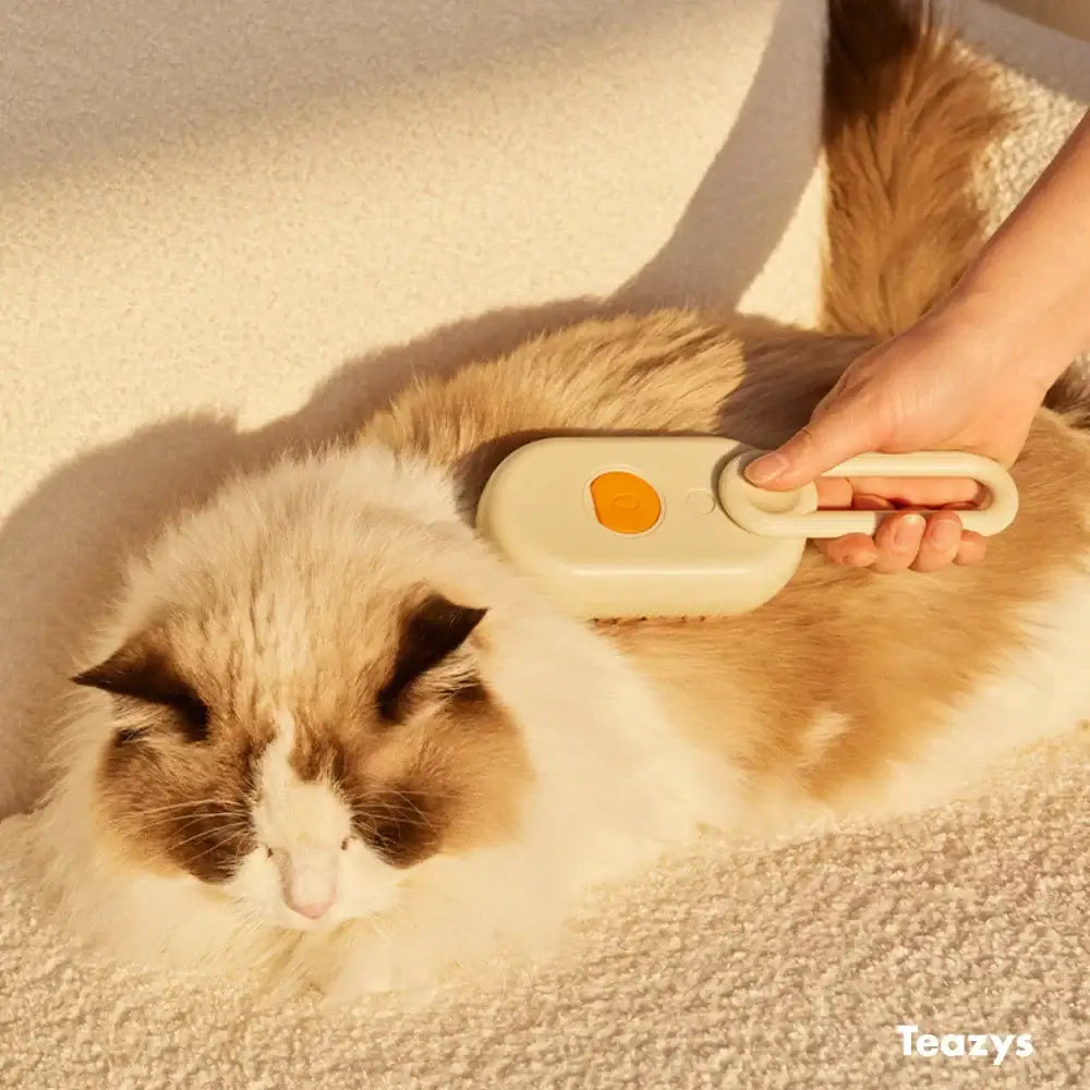 A fluffy cat is being brushed by a person using the CLOUD CARE BRUSH on a light fabric surface, ensuring every strand of fur is pampered to perfection.