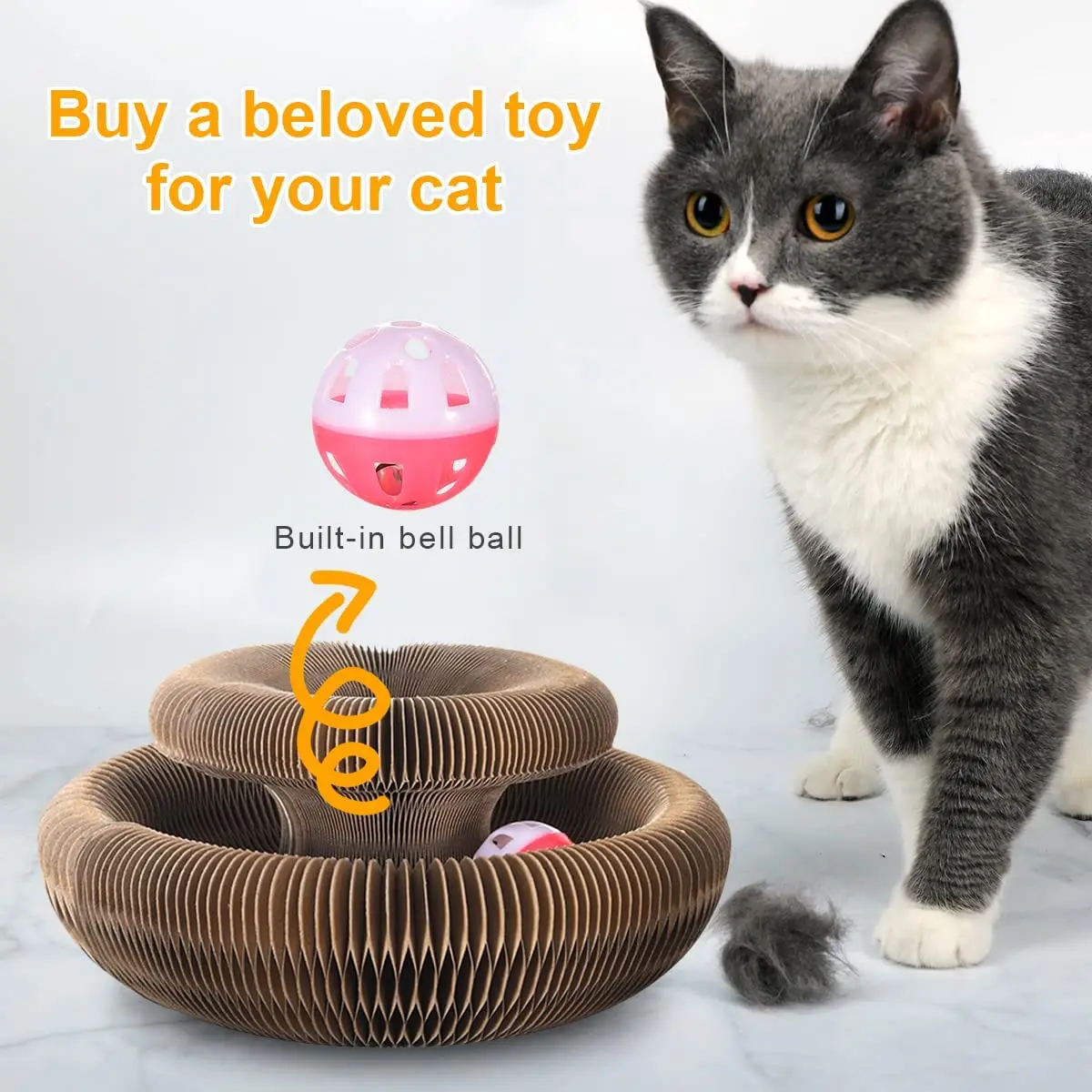 A gray and white cat sits next to the Magic Organ Cat Toy, a spiral cardboard scratcher featuring a built-in bell ball. Text reads "Buy a beloved toy for your cat.